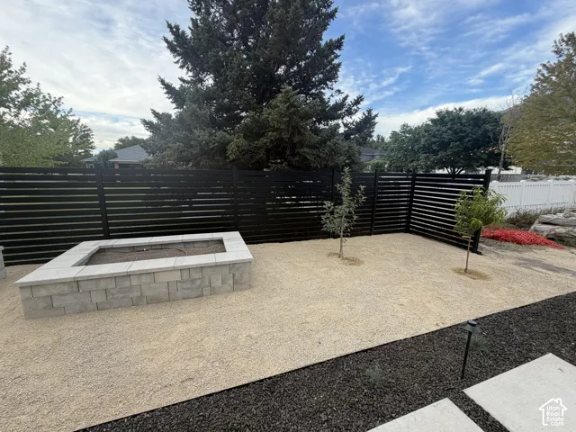 Outdoor living space featuring a rectangular stone fire pit, black slatted fencing, and a gravel-covered yard