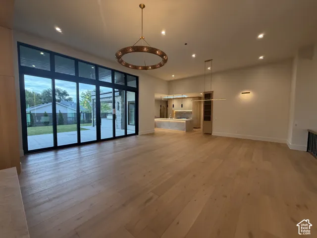 Expansive living area featuring light wood-finish flooring, a full wall of black-framed glass panel doors, and a circular overhead chandelier