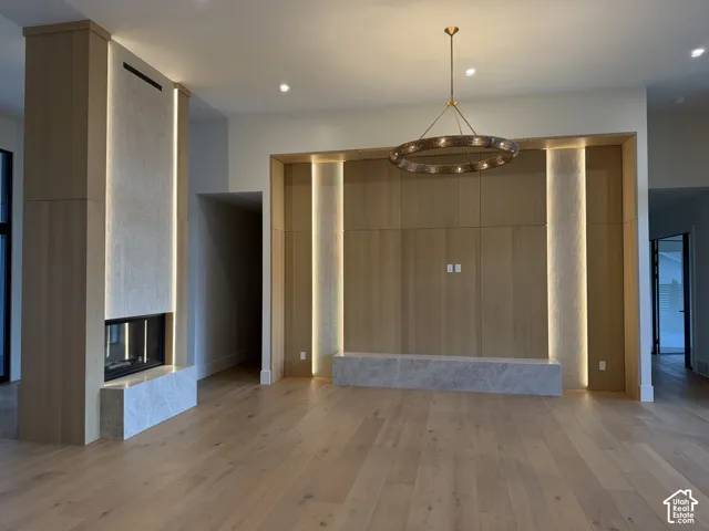 Spacious room featuring light wood-finish flooring, a modern linear fireplace with a stone hearth, and a wood-paneled accent wall with integrated vertical lighting