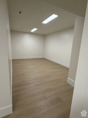 Spacious room featuring wood-finish flooring, white walls, clean white baseboards, and recessed rectangular lighting fixtures