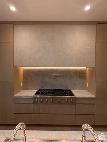 Kitchen featuring a stainless steel range with a pot filler, light wood cabinetry, stone countertops, and a matching stone slab backsplash