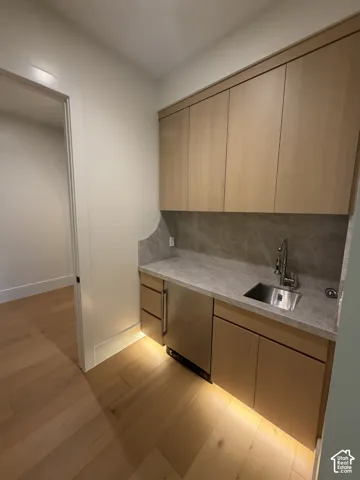 Entrance to primary bedroom. Built-in wet bar featuring light wood-finish cabinetry, a stainless steel sink, a compact under-counter refrigerator, and stone countertops with a matching backsplash