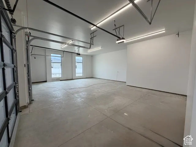 Spacious garage featuring a glass-paneled roll-up door, concrete flooring, overhead fluorescent lighting, and multiple windows