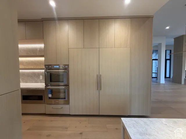 Integrated kitchen wall featuring white oak cabinetry, built-in thermadore stainless steel double ovens, and an integrated 6 ft refrigerator