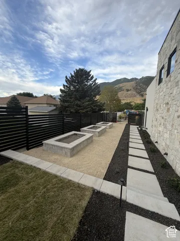 Landscaped side yard featuring three raised garden beds, a stone paver pathway, and a perimeter fence