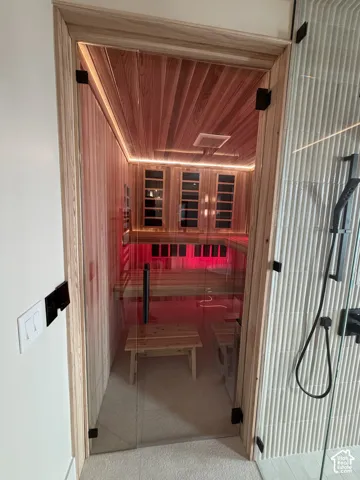 Custom traditional, red light therapy and infra red sauna with clear glass door, wood-paneled walls and ceiling, interior bench seating, and accent lighting