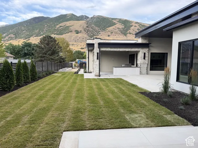 Expansive backyard featuring a manicured lawn, an outdoor kitchen with an integrated grill, and a covered patio area