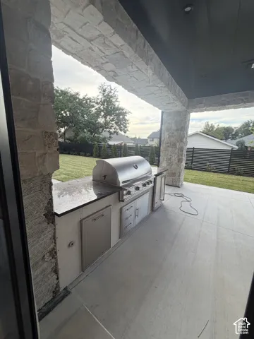 Outdoor kitchen featuring a built-in stainless steel grill, integrated cabinetry, and stone-clad columns