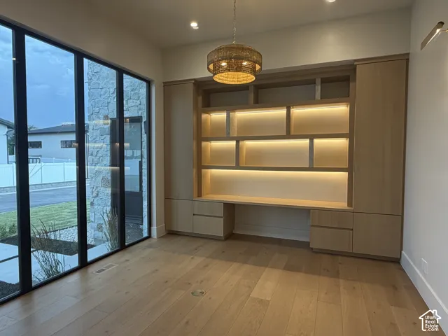 Built-in cabinetry with integrated lighting and desk area, wood-finish flooring, floor-to-ceiling windows with black frames, and a woven pendant light fixture