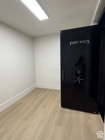 Dedicated interior room featuring a "Fort Knox" safe, wood-finish flooring, white baseboards, white walls, and a ceiling-mounted rectangular light fixture