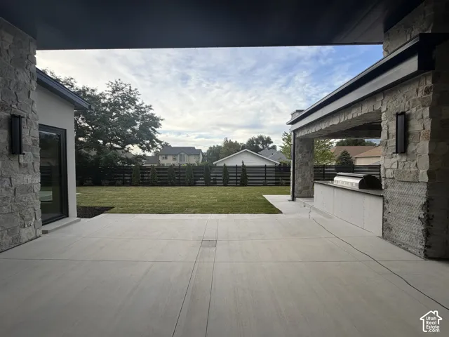 Expansive concrete patio offering an outdoor kitchen with integrated grill and a stone-clad exterior