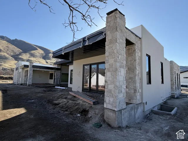 Back of property with stucco, a mountain view, a patio, and natural stone. View of the primary bedroom with it's own private covered patio