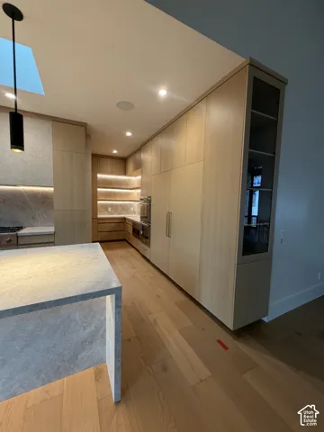 Kitchen featuring light wood-finish cabinetry, integrated appliances, and a waterfall-edge island with a stone-finish countertop