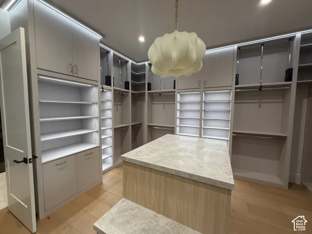 Expansive custom closet featuring an integrated island with a stone-finish countertop, extensive built-in cabinetry, recessed and accent lighting, wood-finish flooring, and a unique pendant light fixture