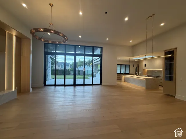 Spacious interior featuring wide plank wood-finish flooring, a large patio door system, a contemporary circular chandelier, recessed lighting, and a modern kitchen with an oversized island and linear pendant lighting