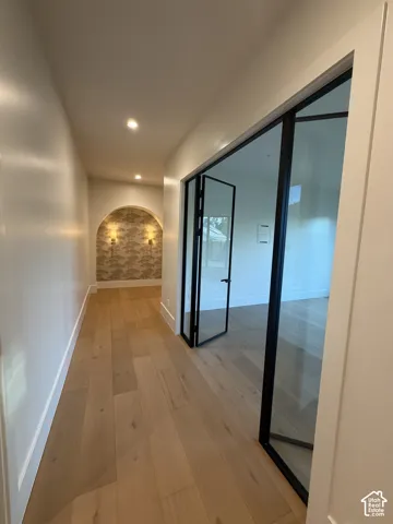 Entryway hallway featuring wide plank wood-finish flooring, recessed lighting, and a decorative arched niche with sconces.  Flex room and hallway to primary bedroom