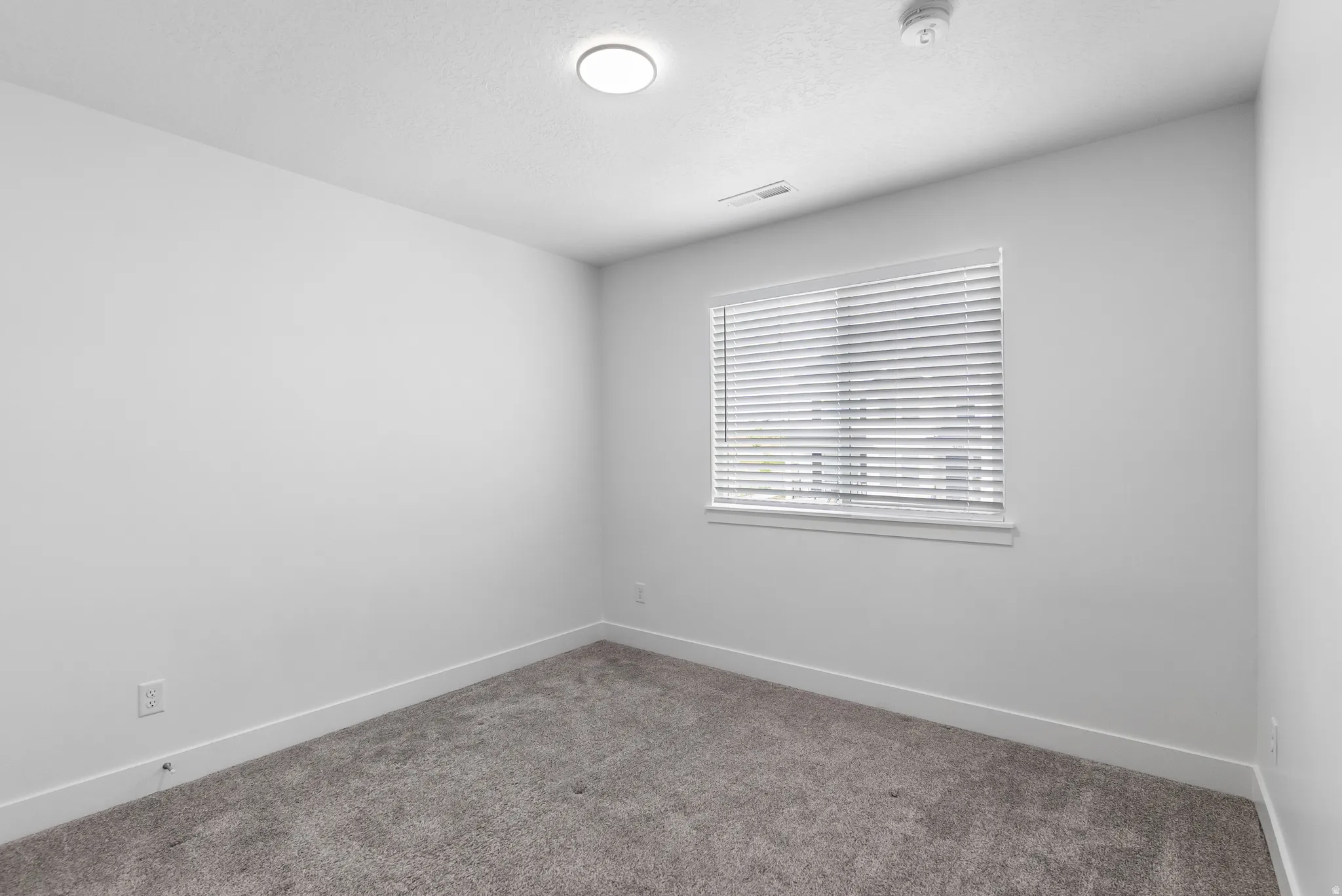Unfurnished room with carpet floors, a textured ceiling, and a smoke detector