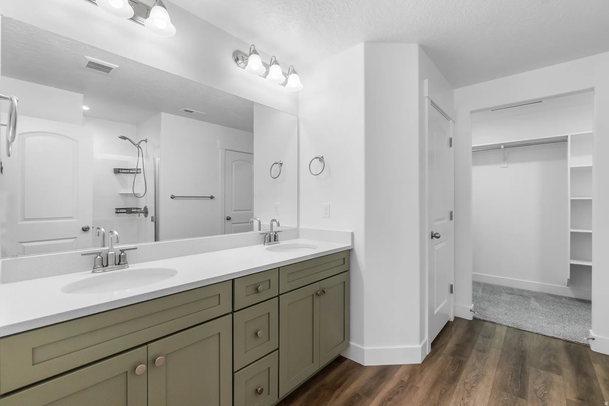 Bathroom featuring a walk in closet, double vanity, a textured ceiling, walk in shower, and dark wood-style floors