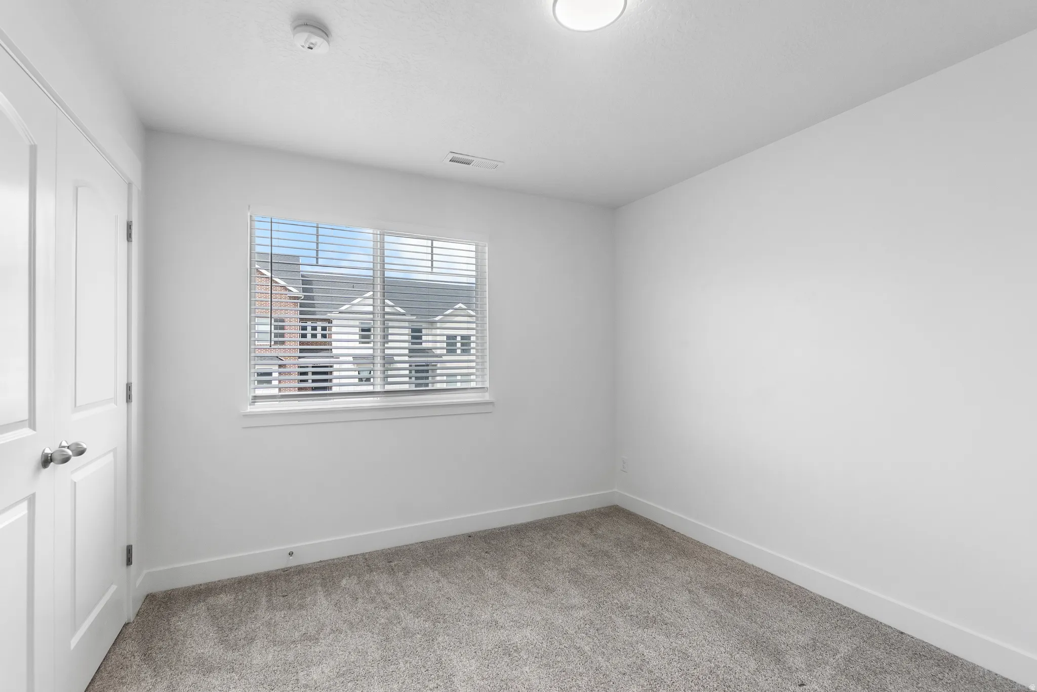 Empty room featuring light colored carpet and a smoke detector