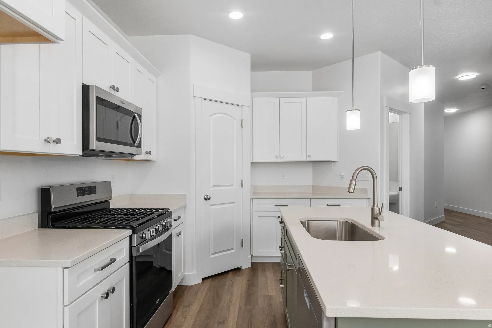 Kitchen featuring stainless steel appliances, a kitchen island with sink, dark wood-style floors, and white cabinetry