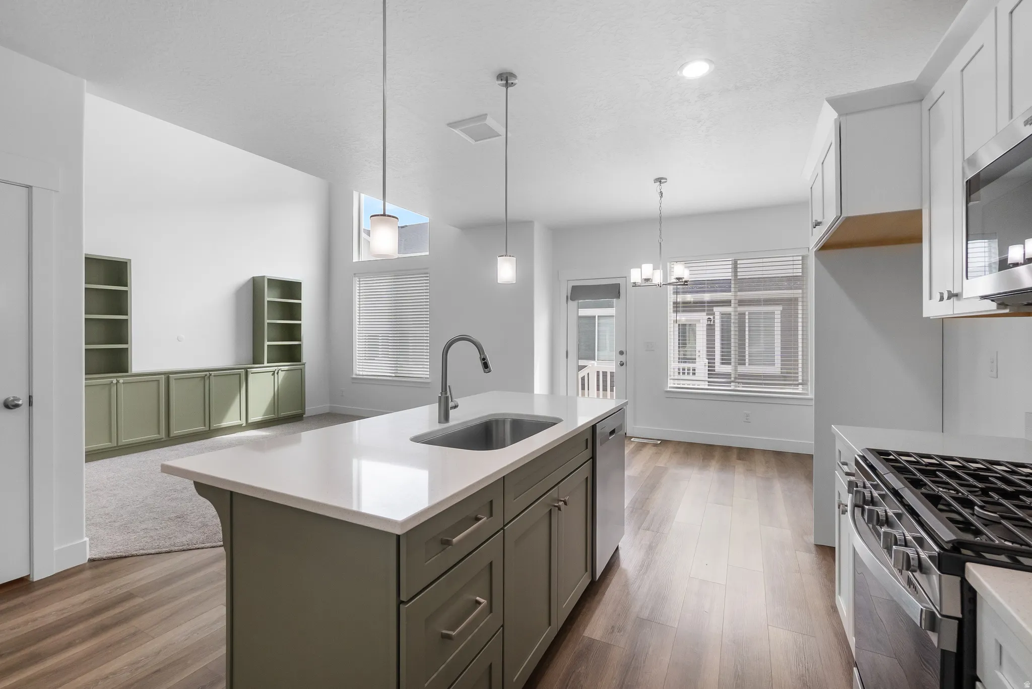 Kitchen featuring light stone counters, a kitchen island with sink, stainless steel appliances, light wood-type flooring, and suspended lighting