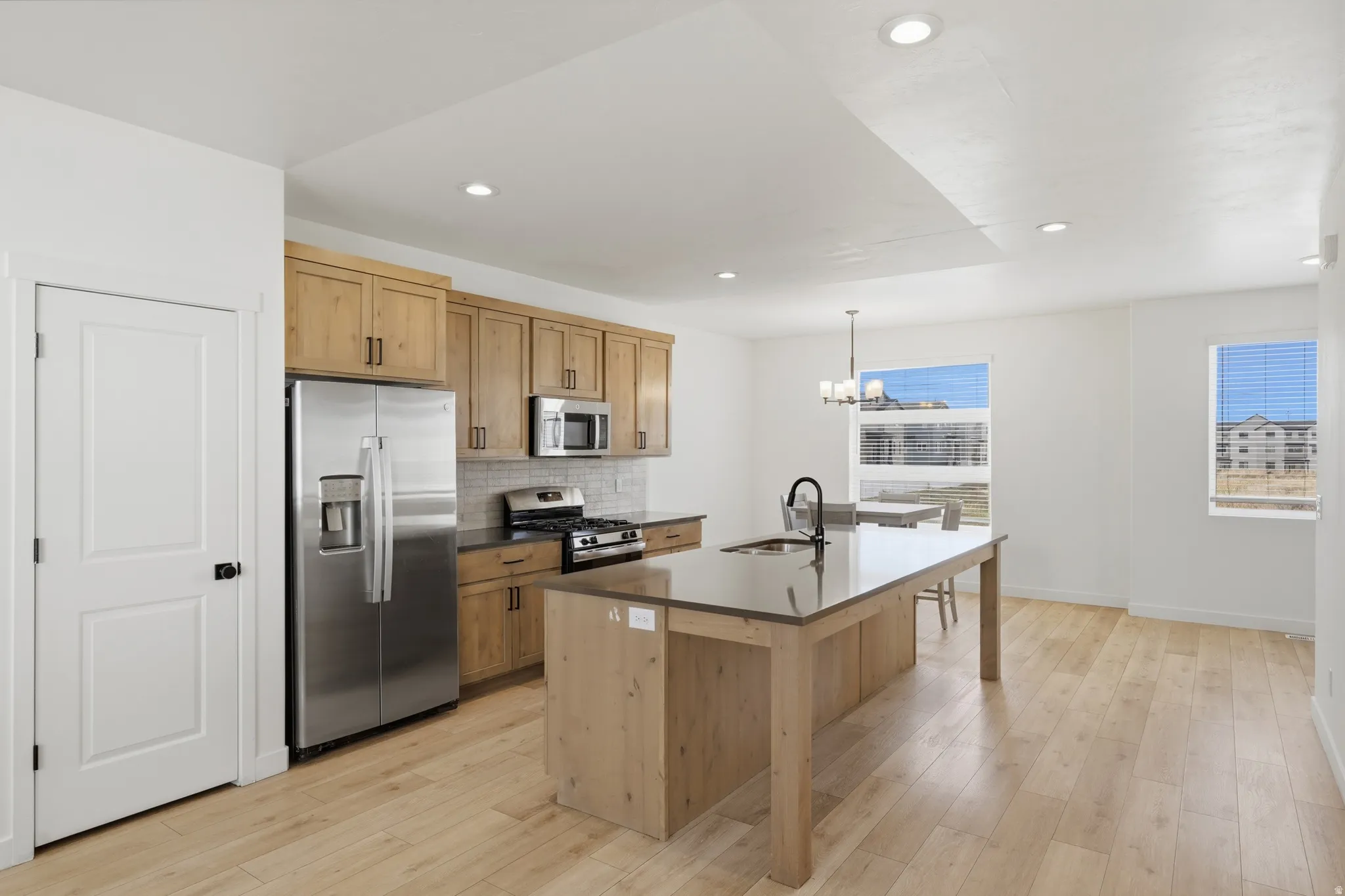 Kitchen featuring stainless steel appliances, light wood-style floors, a center island with sink, and a chandelier