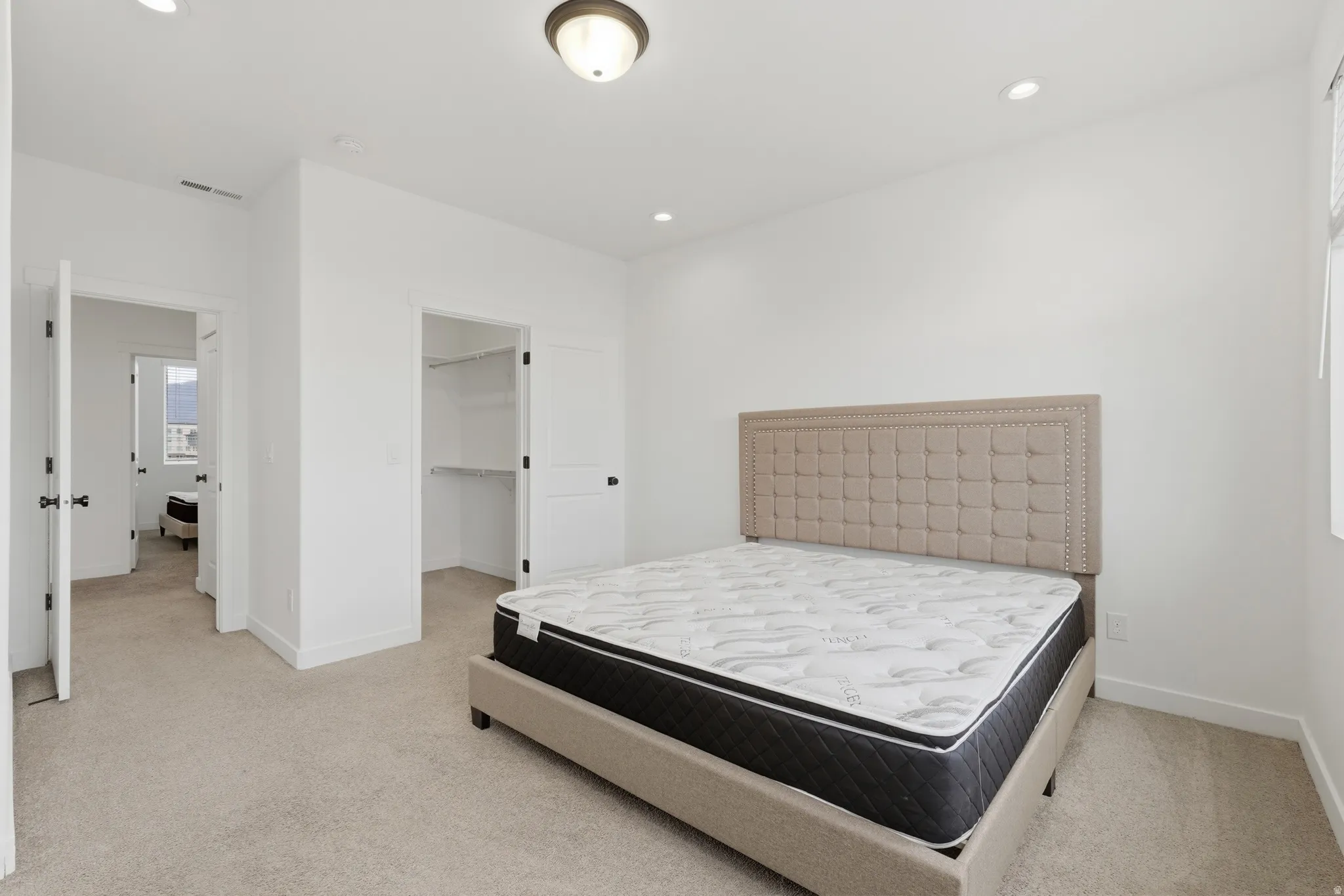 Bedroom featuring light colored carpet, a walk in closet, and recessed lighting