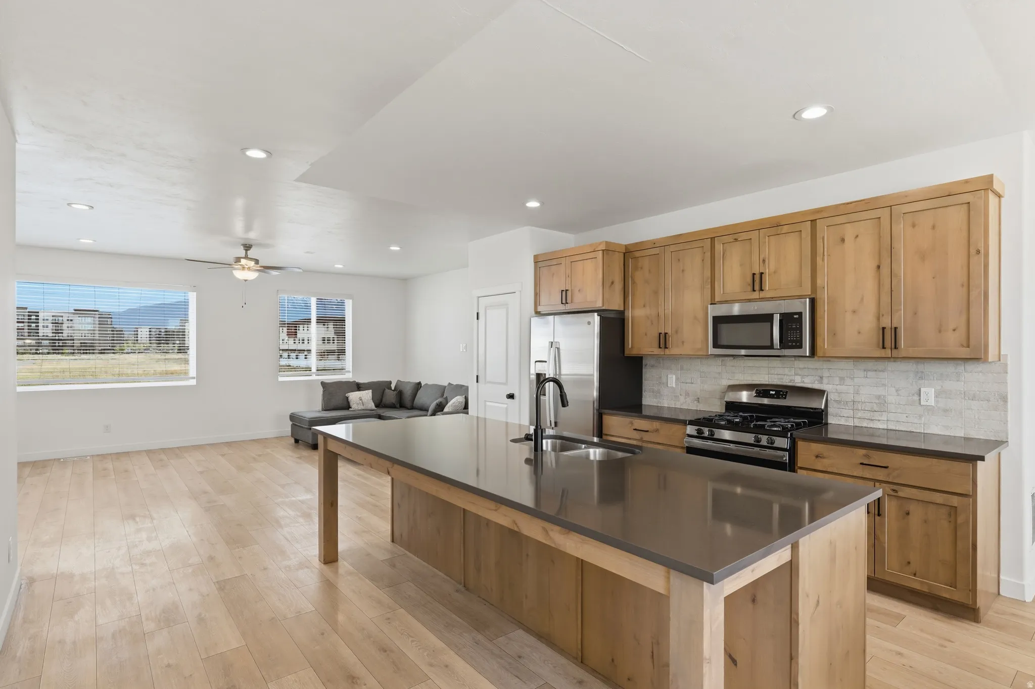 Kitchen with stainless steel appliances, open floor plan, a center island with sink, light wood-style flooring, and decorative backsplash