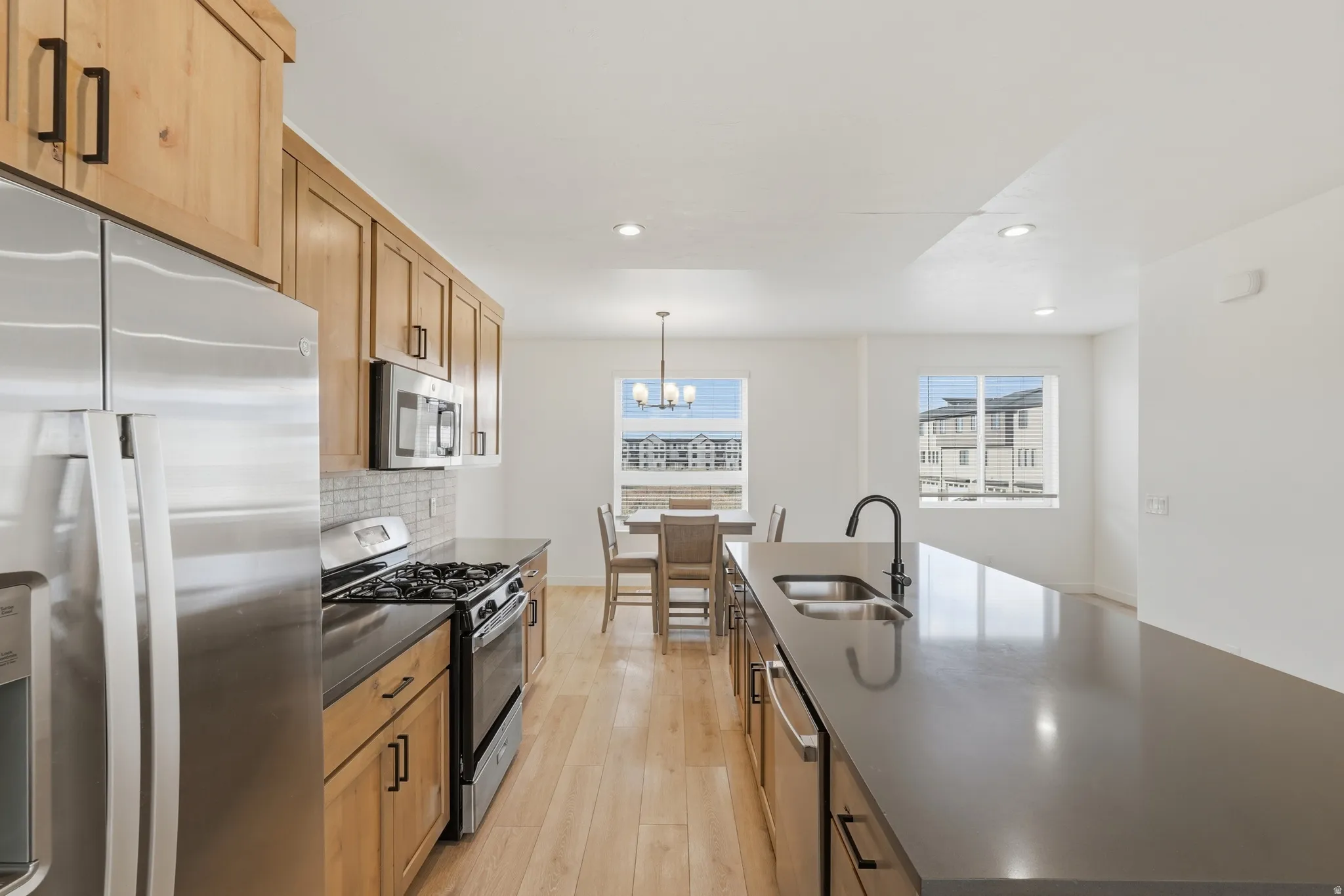 Kitchen with stainless steel appliances, light wood-style flooring, an island with sink, decorative backsplash, and a chandelier