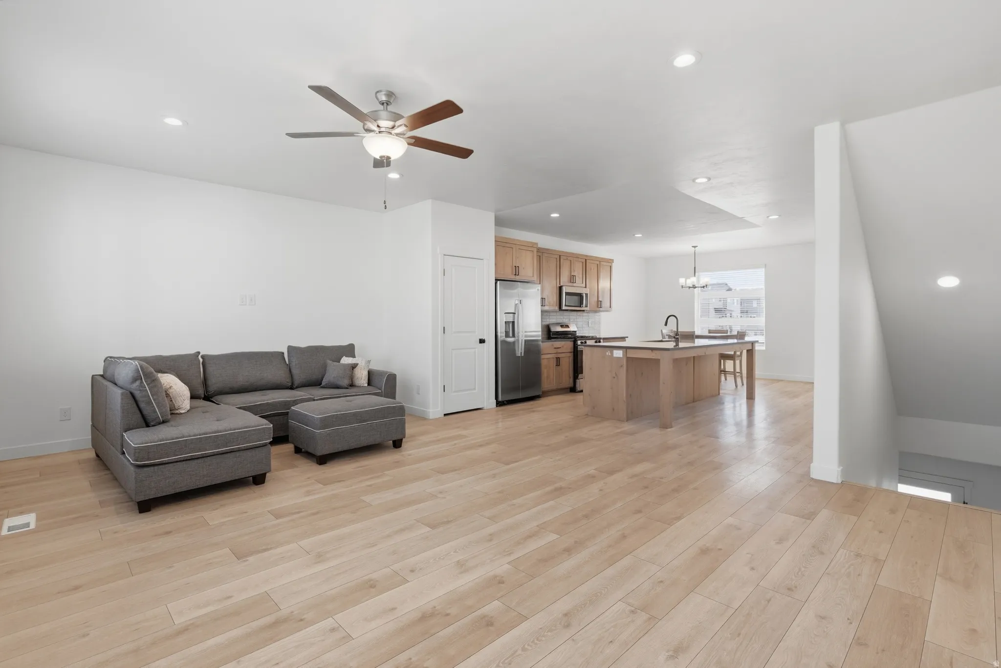 Living room featuring a ceiling fan, light wood-style flooring, and suspended lighting