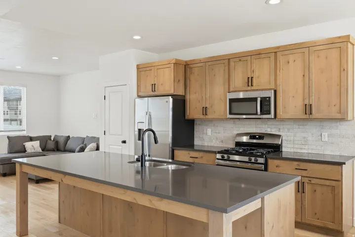 Kitchen with stainless steel appliances, light wood finished floors, an island with sink, open floor plan, and light wood finish cabinets