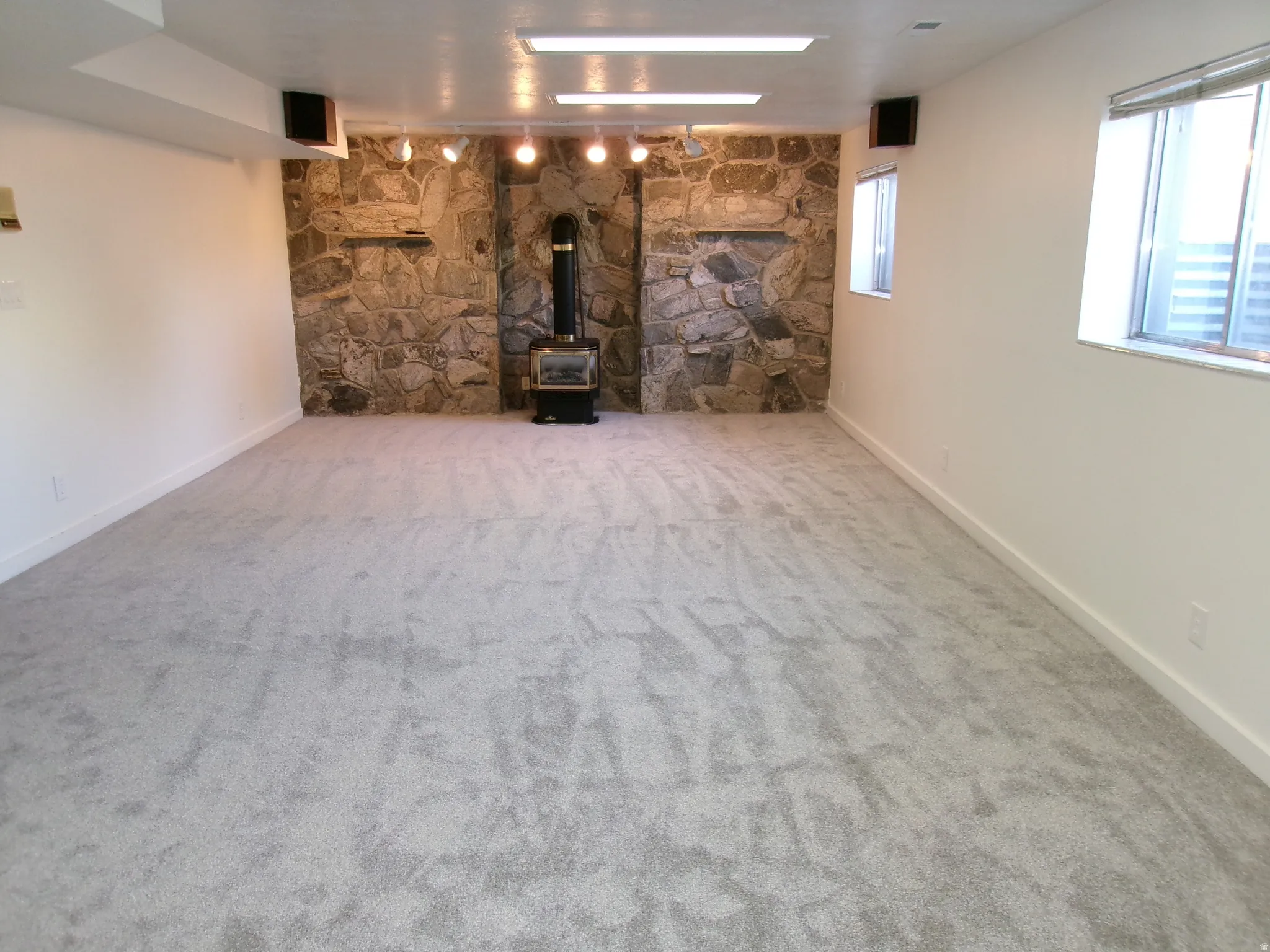 Basement living room with a wood stove, light carpet, and rail lighting 14 x 24