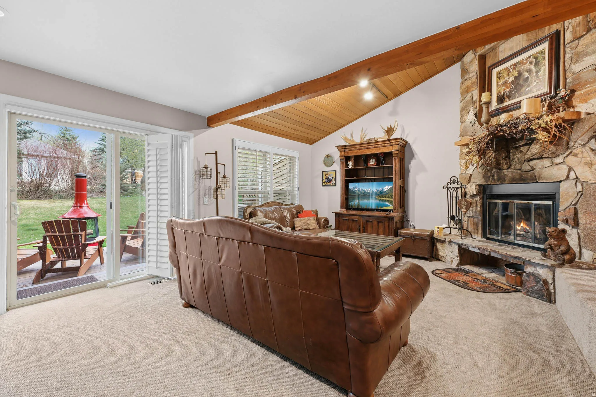 Carpeted living room with a fireplace, lofted ceiling with beams, and wooden ceiling