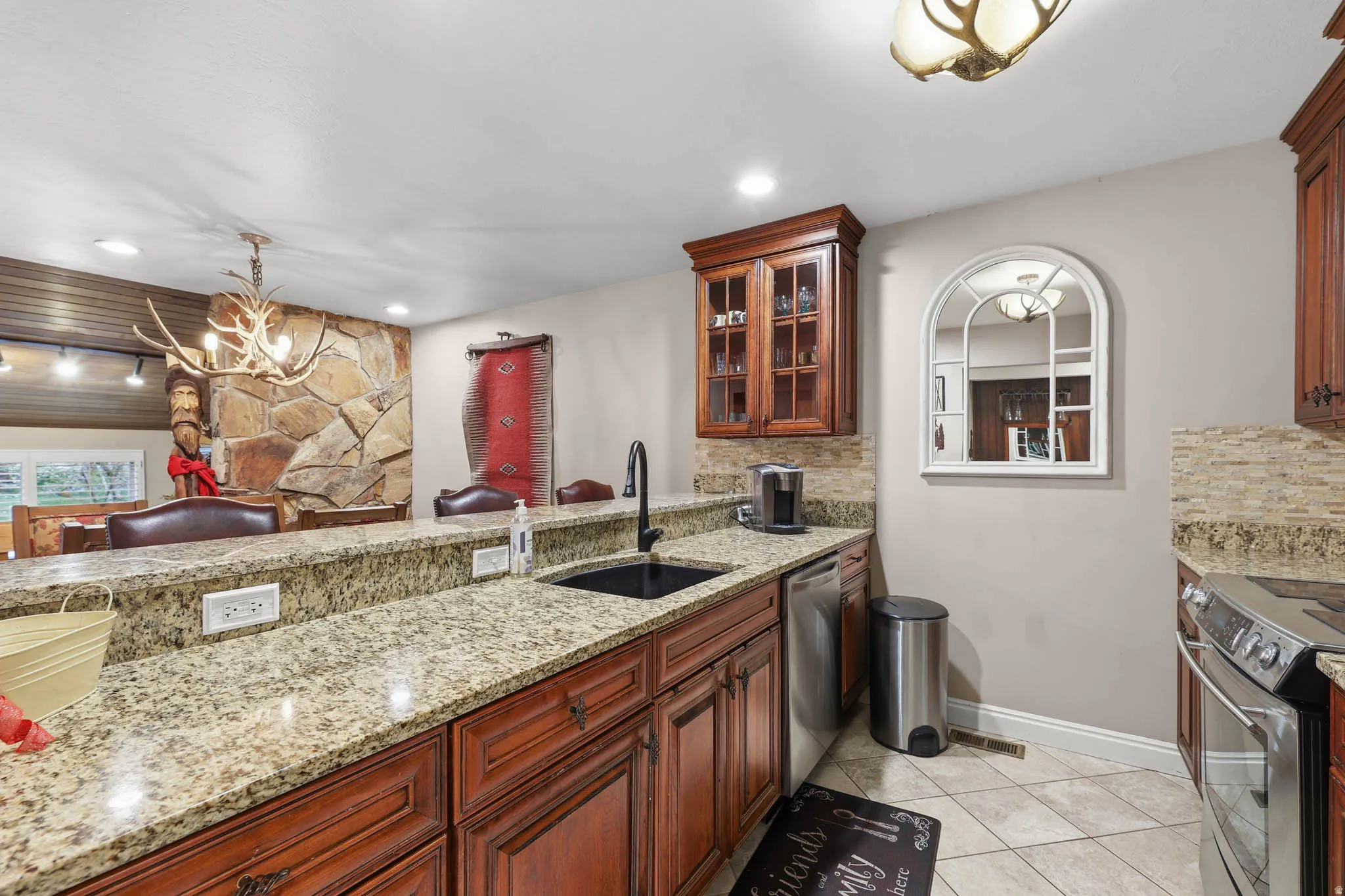 Kitchen featuring glass fronted cabinets, stainless steel appliances, light tile patterned floors, light stone counters, and backsplash