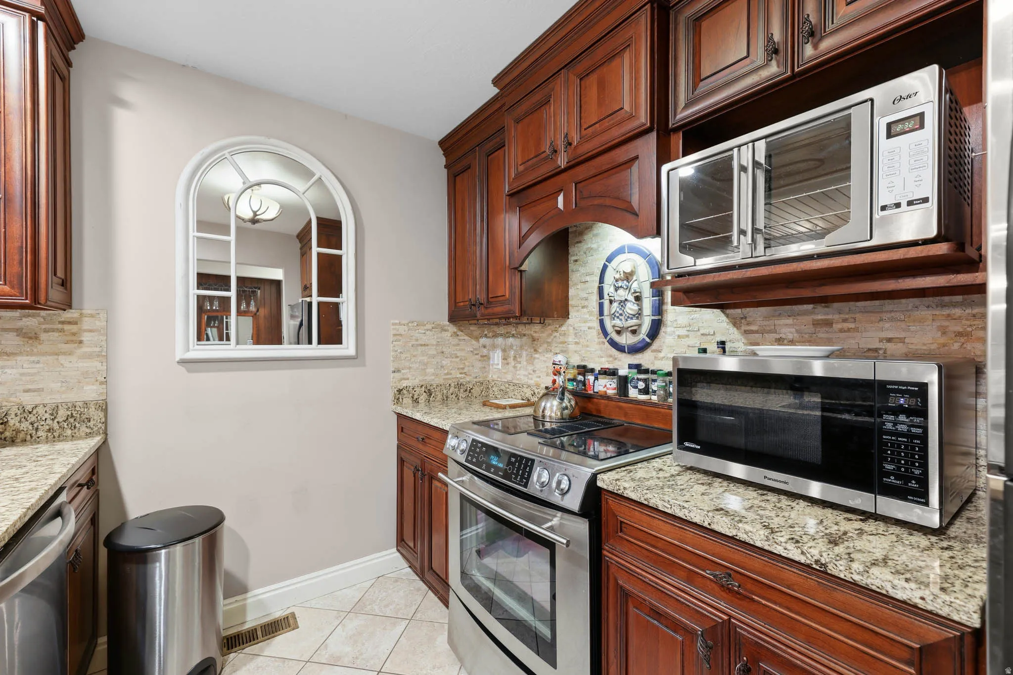 Kitchen with stainless steel appliances, light stone countertops, light tile patterned floors, and decorative backsplash
