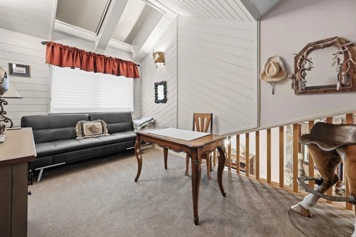 Office area featuring wooden walls, carpet flooring, and vaulted ceiling with beams