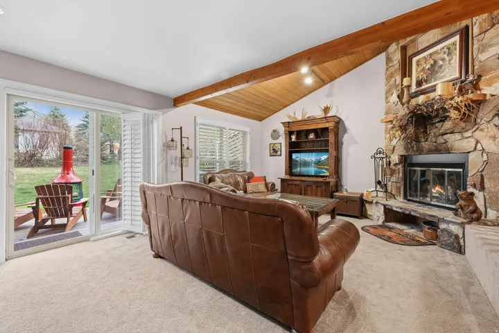 Carpeted living room with a fireplace, lofted ceiling with beams, and wooden ceiling