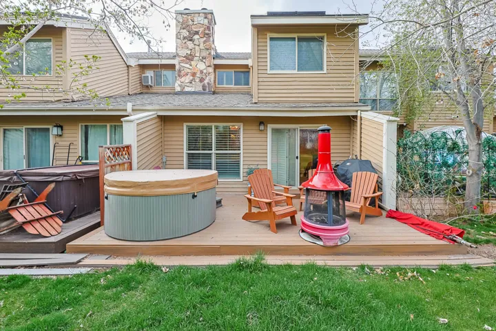 Back of house with a hot tub, a shingled roof, a wooden deck, and a chimney