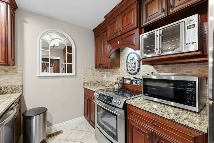 Kitchen with stainless steel appliances, light stone countertops, light tile patterned floors, and decorative backsplash