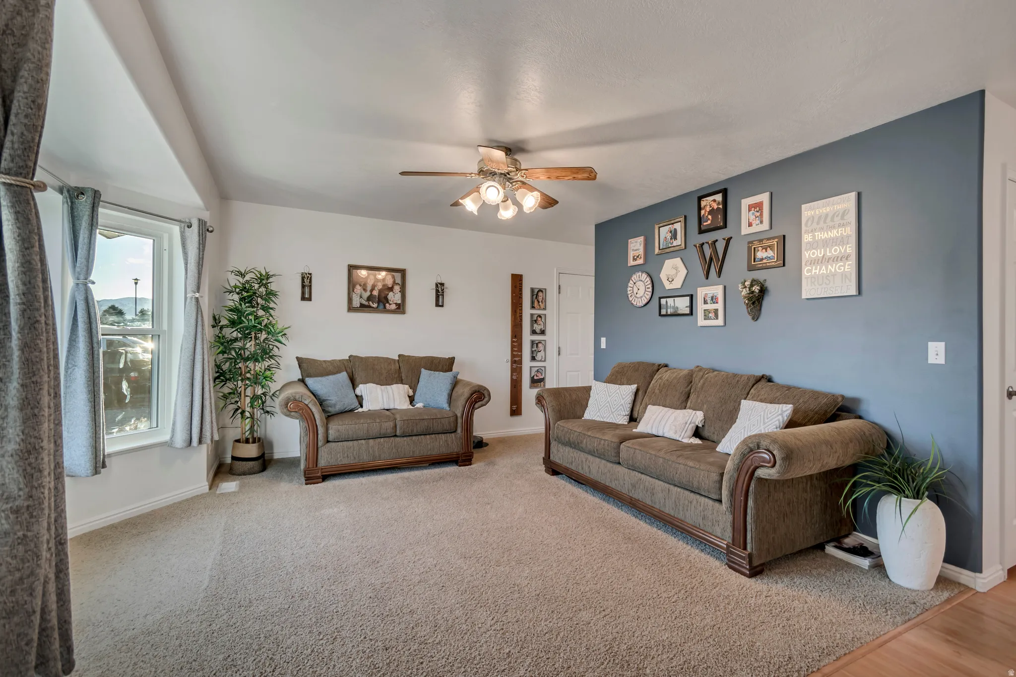 Carpeted living area with a ceiling fan and baseboards