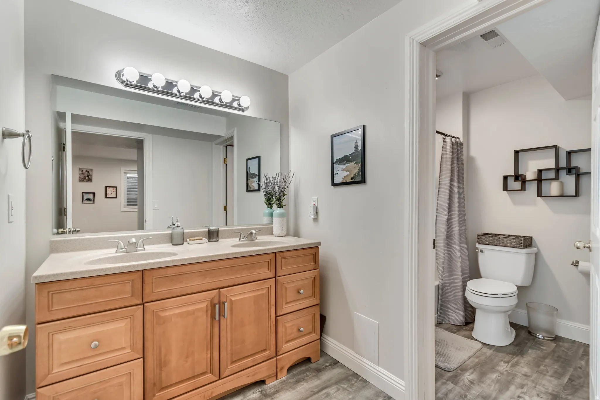 Full bath featuring double vanity, light wood-style floors, and a textured ceiling