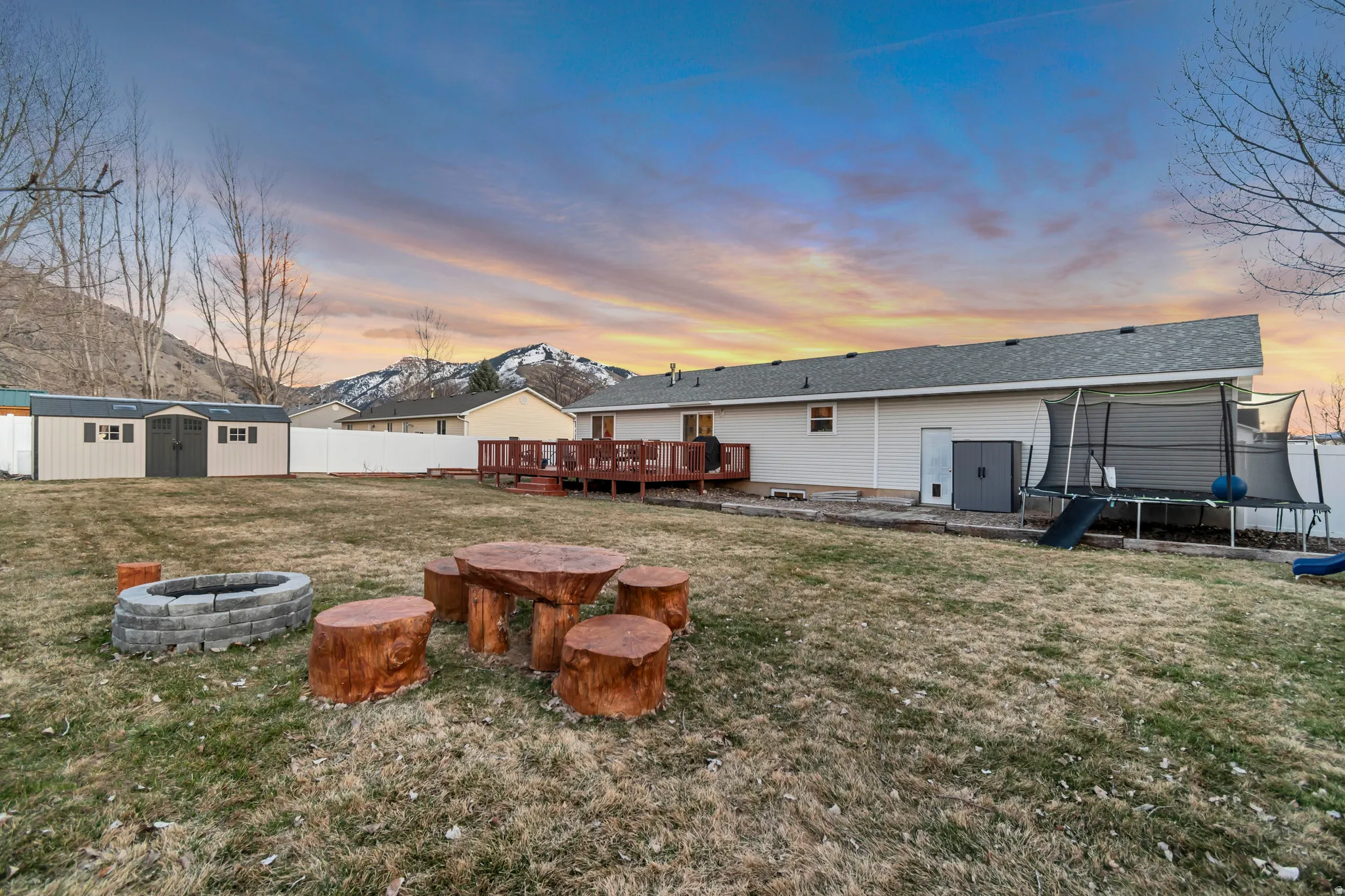 Back of house at dusk featuring a shed, a trampoline, an outdoor fire pit, a deck with mountain view, and a fenced backyard