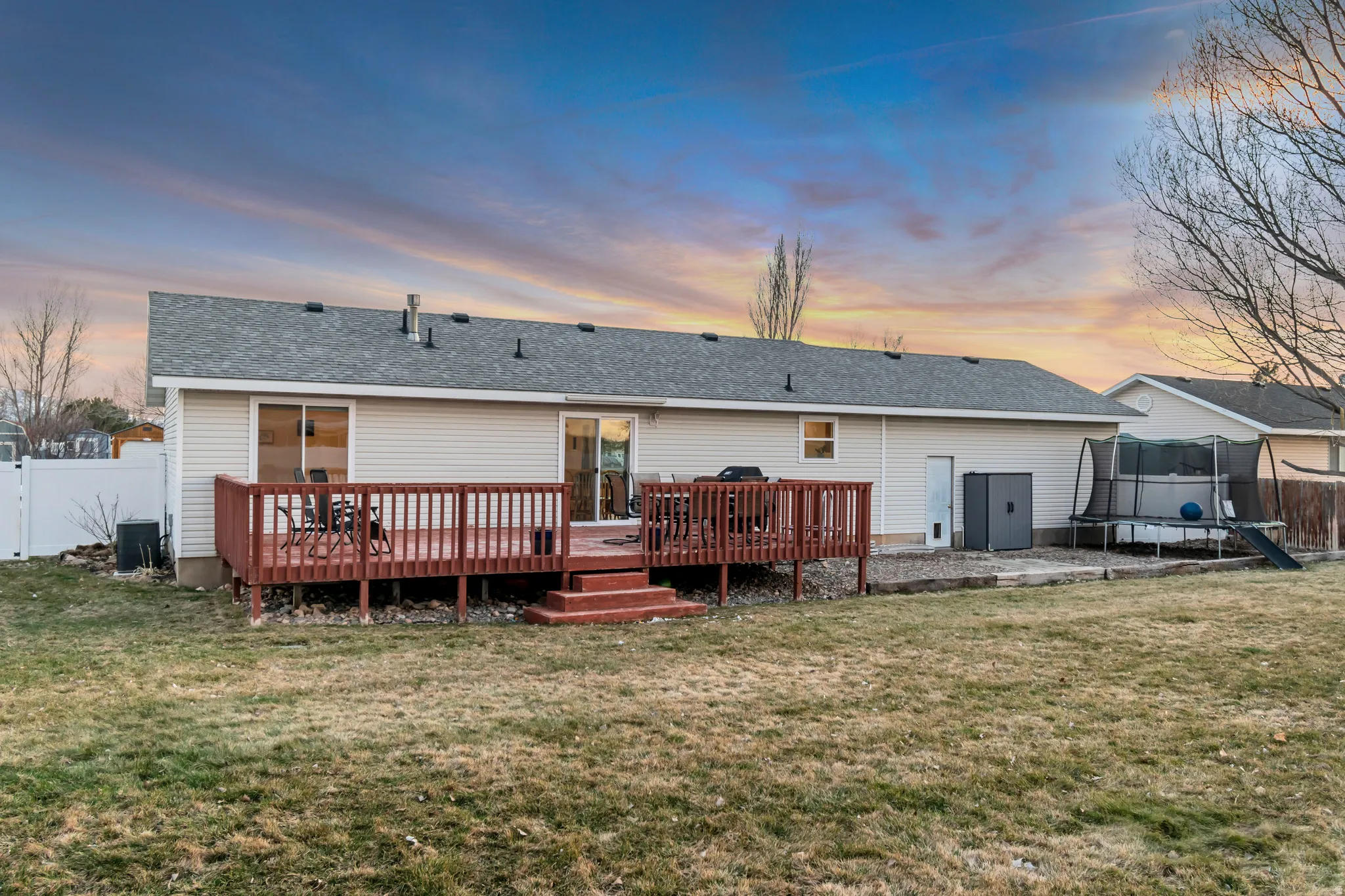 Back of property with a fenced backyard, a trampoline, a shingled roof, and a deck