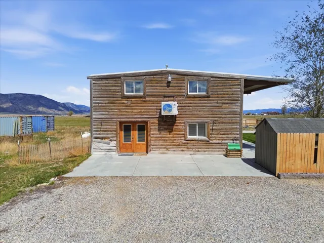 Back of house featuring a mountain view, a storage unit, a patio area, and log siding