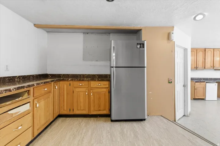 Kitchen with freestanding refrigerator, white dishwasher, a textured ceiling, and wood finish cabinetry