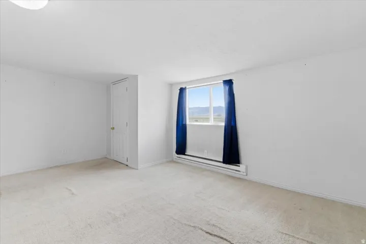 Spare room with baseboard heating and light colored carpet