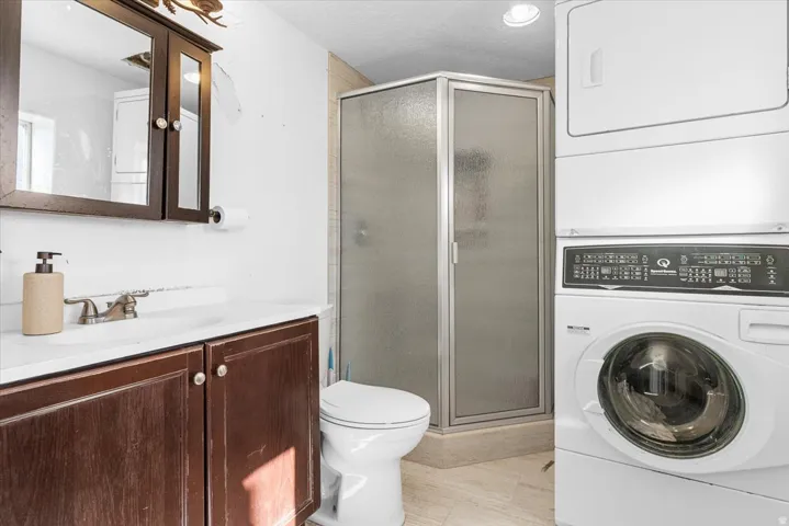 Bathroom featuring vanity, a stall shower, stacked washing machine and dryer, and a textured ceiling
