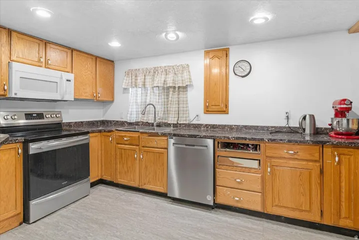 Kitchen with stainless steel appliances, wood finish cabinetry, a textured ceiling, recessed lighting, and dark stone countertops