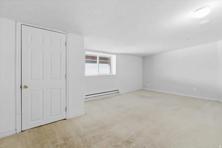 Unfurnished room featuring a textured ceiling, light colored carpet, and a baseboard radiator