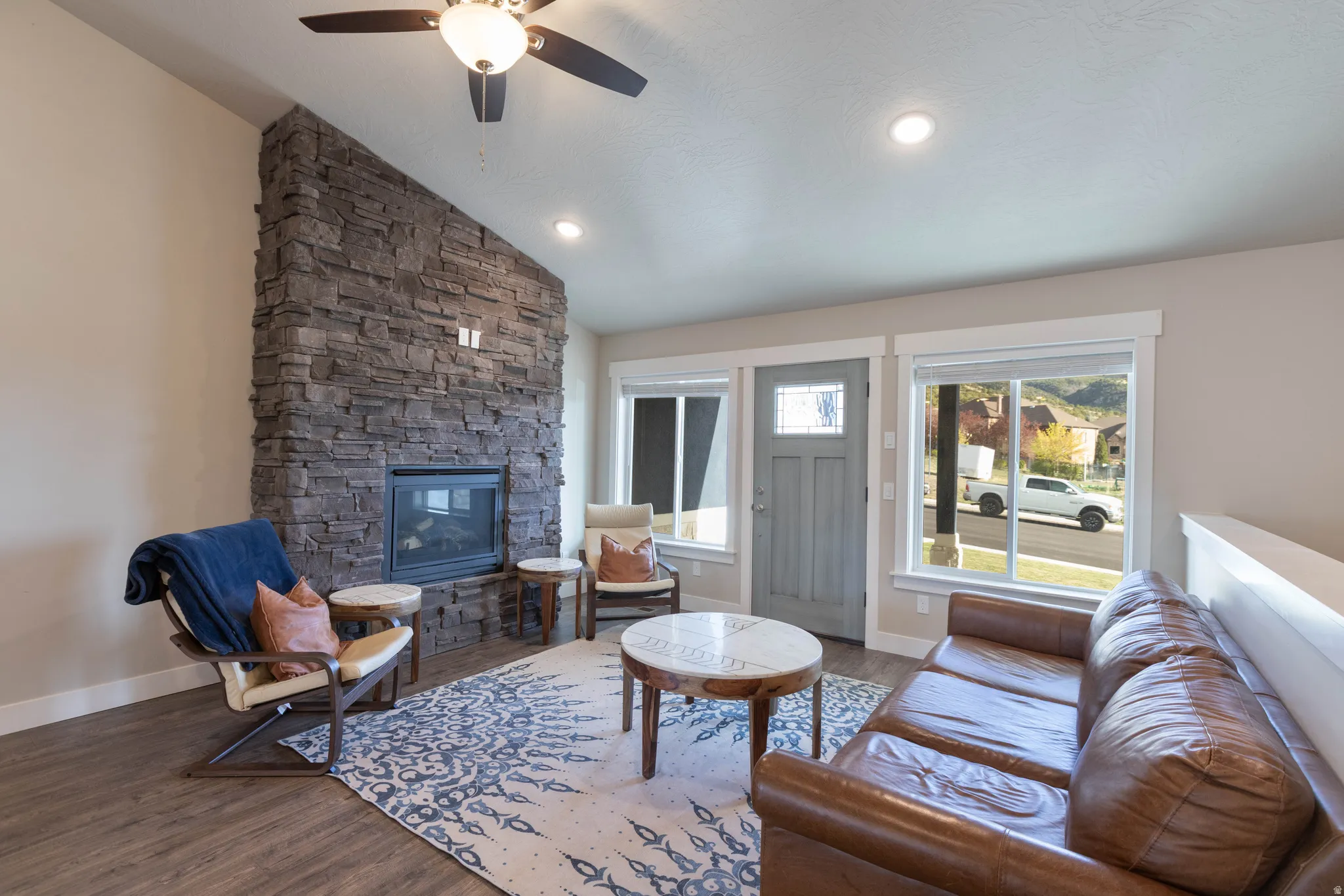 Living area with vaulted ceiling, a stone fireplace, wood finished floors, and ceiling fan
